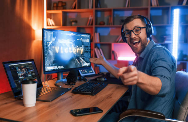 uplifting and energized man is playing the shooter game on his computer. neon lighting - 電競 個照片及圖片檔